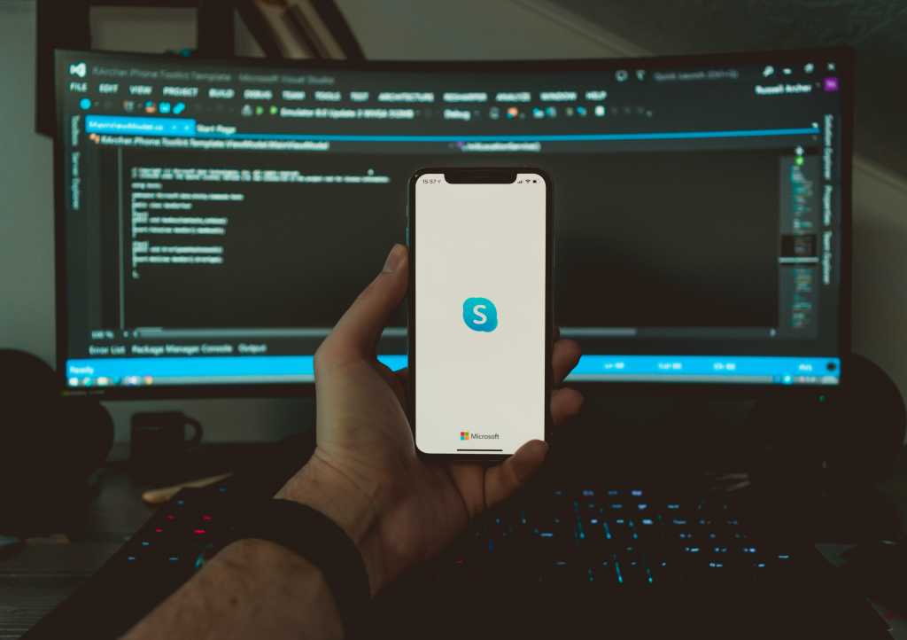 Male hand holding a phone in front of a computer monitor with the Skype app open